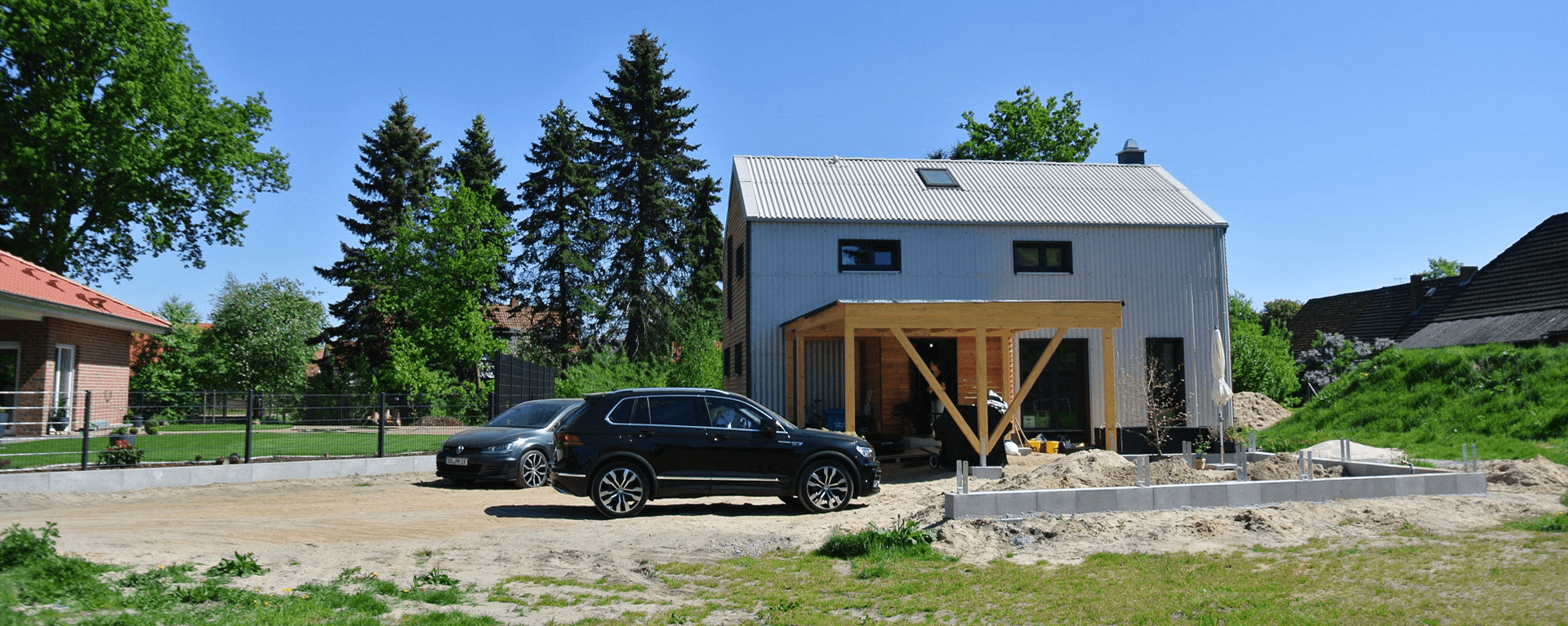 Die klare Form des Hauses und die verwendeten, einfachen Fassadenmaterialien Holz und Faserzement-Wellplatte fügen es in die nähere Umgebung ein.